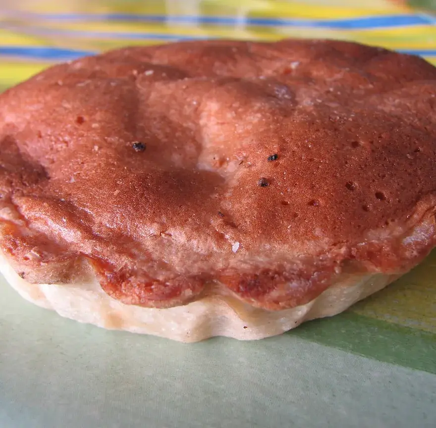 Tourment d’amour, tartelette ronde à la croûte dorée et au biscuit bombé, posée sur une nappe colorée