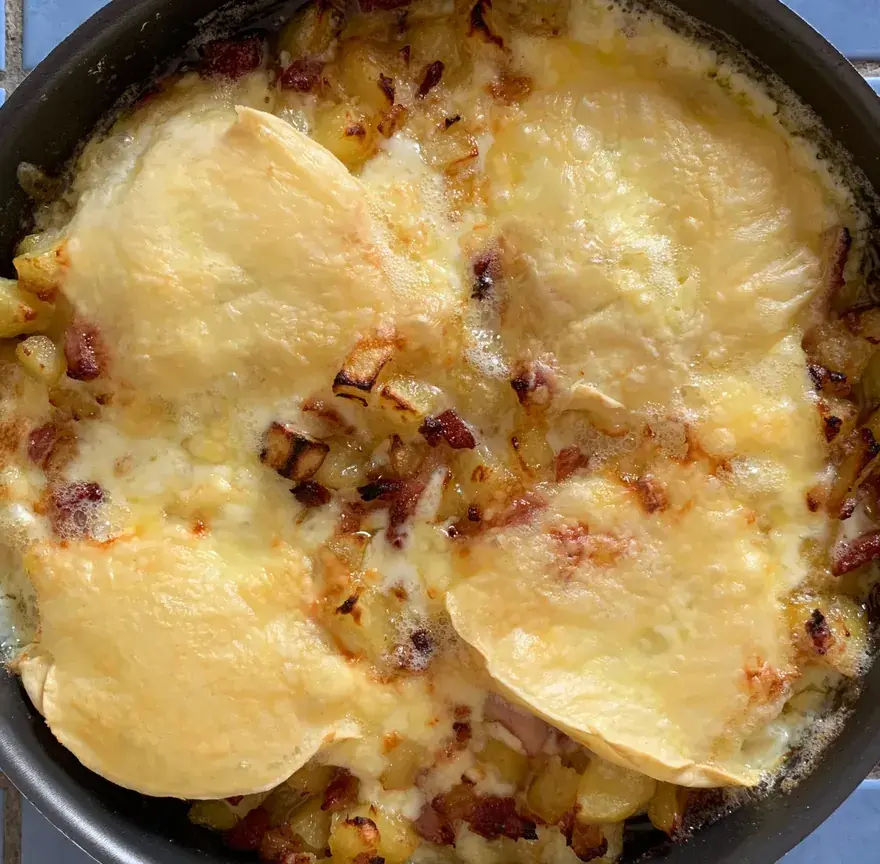 Tartiflette sortie du four dans une poêle, reblochon fondu et doré sur les pommes de terre, lardons et oignons