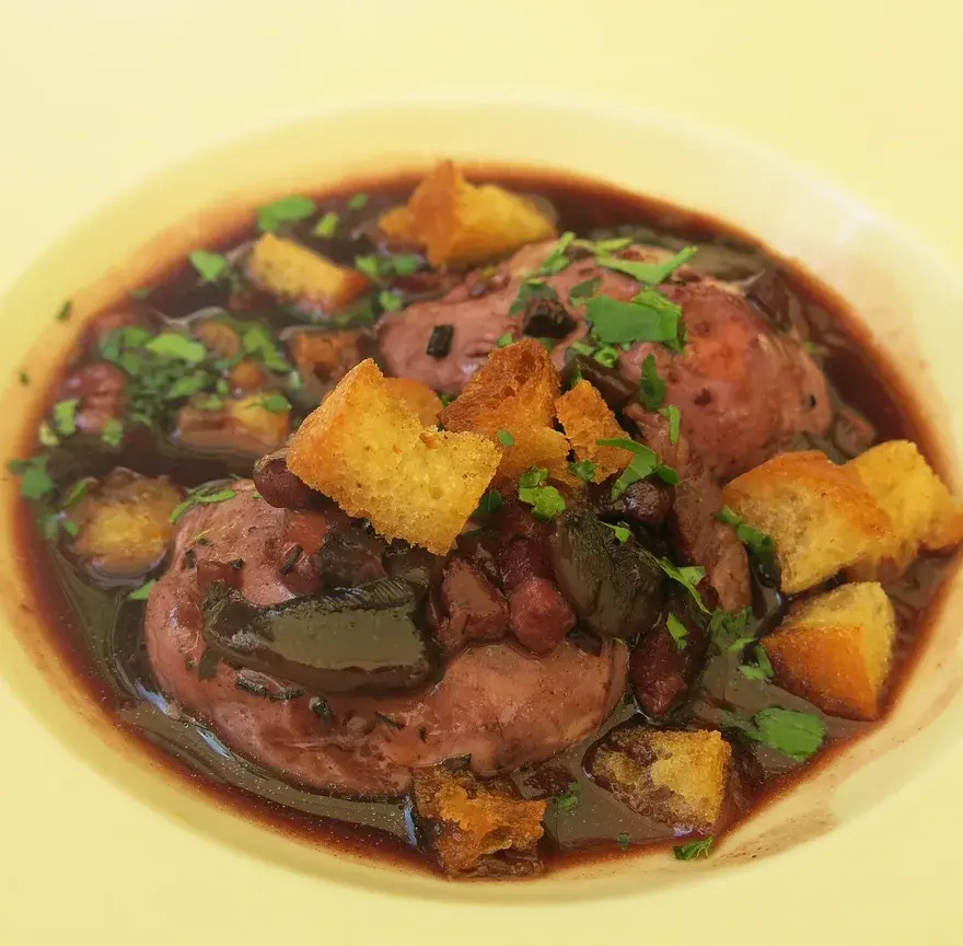 Œufs en meurette servis dans une assiette creuse, nappés de sauce au vin rouge avec lardons, croûtons et persil