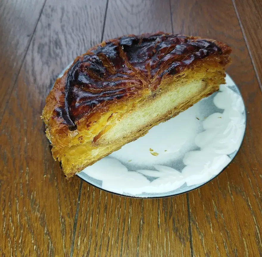 Part de pithiviers feuilleté à la croûte dorée et brillante, garni de crème d’amandes, posée sur une assiette