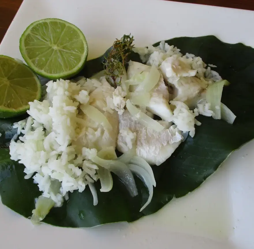 Blaff de poisson servi sur une feuille, avec des oignons fondants, des herbes et des demi-citrons verts