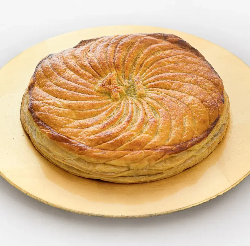 Galette feuilletée à la frangipane, bien dorée et décorée d’une rosace, posée sur un carton doré