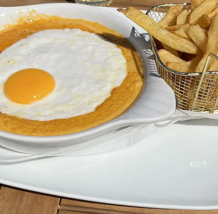 Welsh gratiné au cheddar servi dans un plat, un œuf au plat sur le dessus et un panier de frites à côté