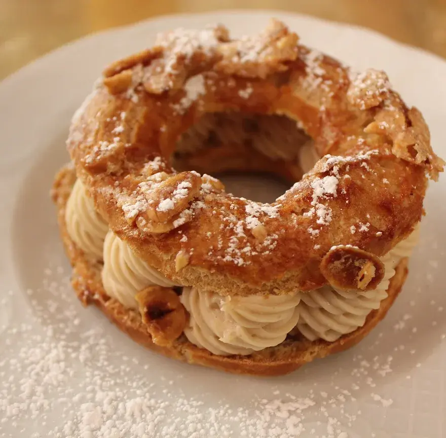 Paris-brest en couronne, pâte à choux dorée aux amandes effilées garnie de crème au praliné, saupoudré de sucre glace