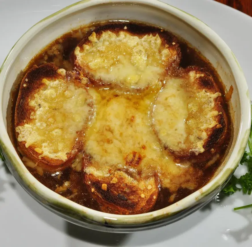 Bol de soupe à l’oignon recouvert de tranches de pain et de fromage fondu et gratiné, avec quelques brins de persil