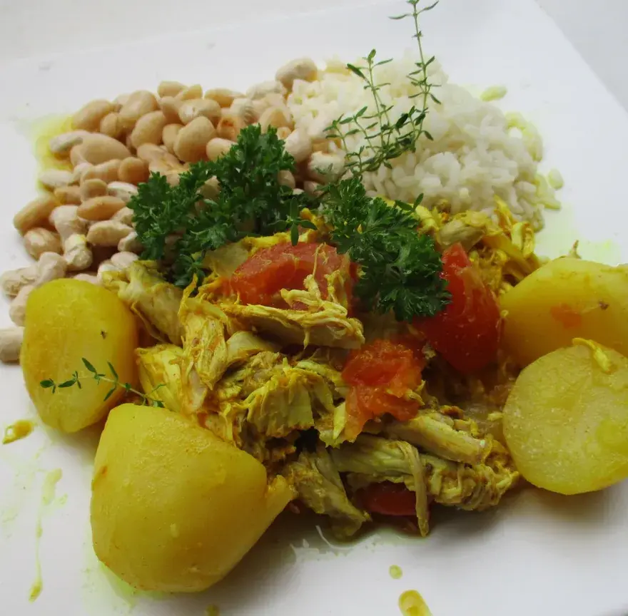Assiette de cari poulet à la sauce jaune au curcuma, avec pommes de terre, riz blanc et haricots blancs