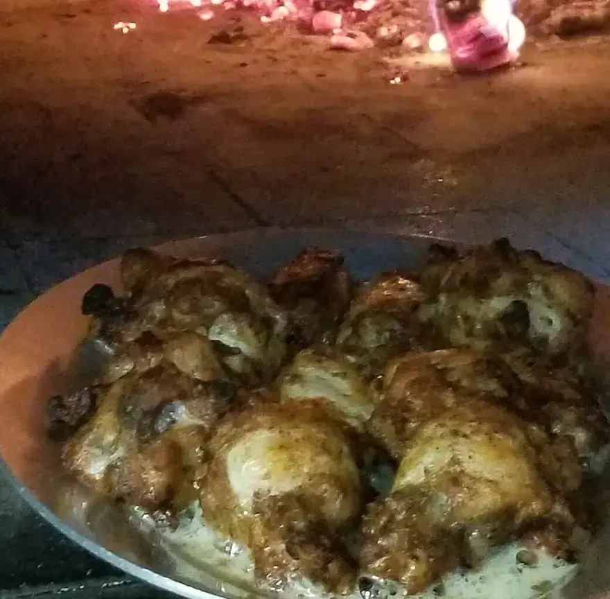 Ailes de poulet grillées et dorées, servies dans un plat près des braises d’un feu de bois
