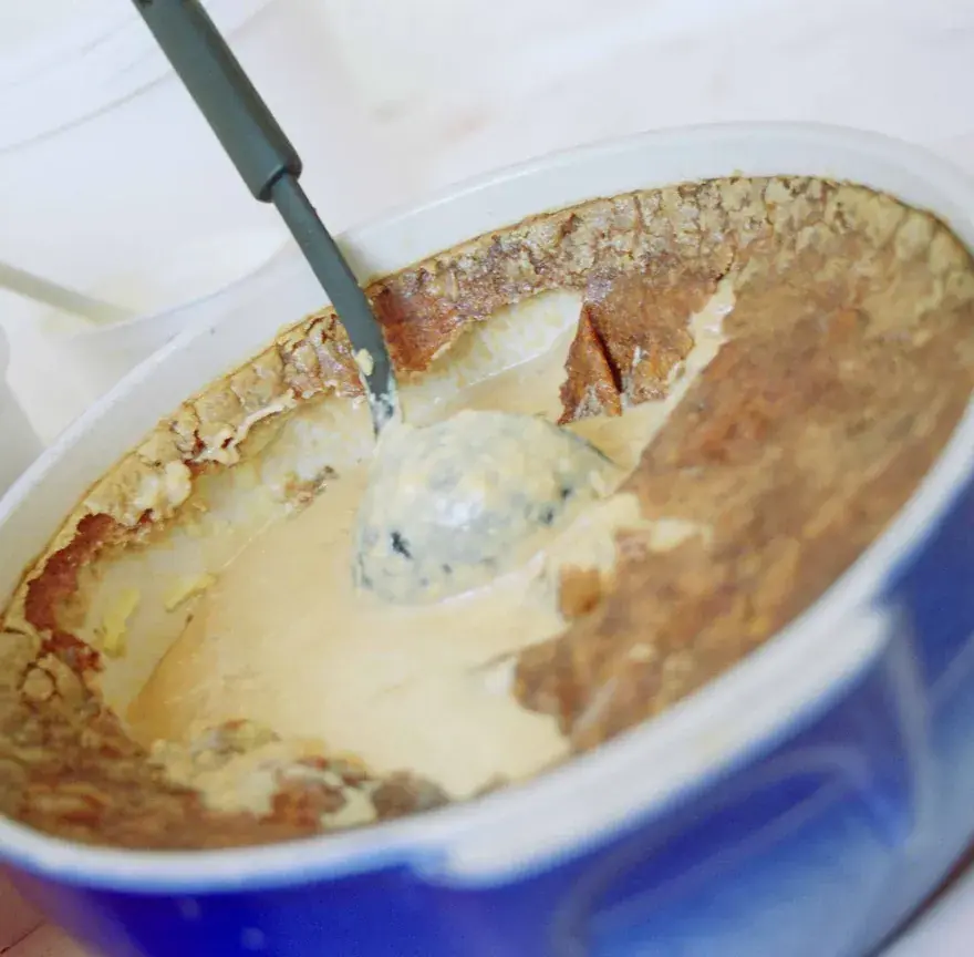 Teurgoule dans une terrine bleue, une cuillère plongée dans le riz au lait crémeux sous sa croûte brune à la cannelle