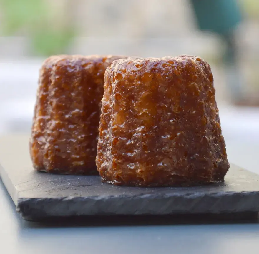 Deux canelés à la croûte brune caramélisée posés sur une plaque d’ardoise