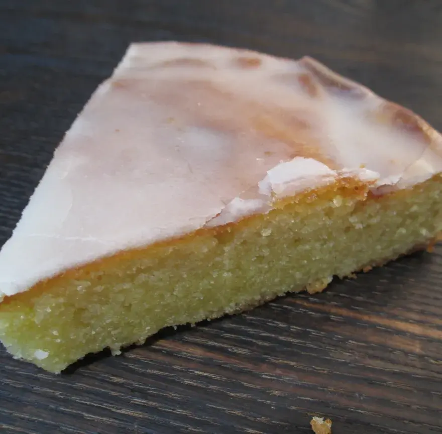 Part de gâteau nantais au cœur jaune et moelleux, recouverte d’un glaçage blanc